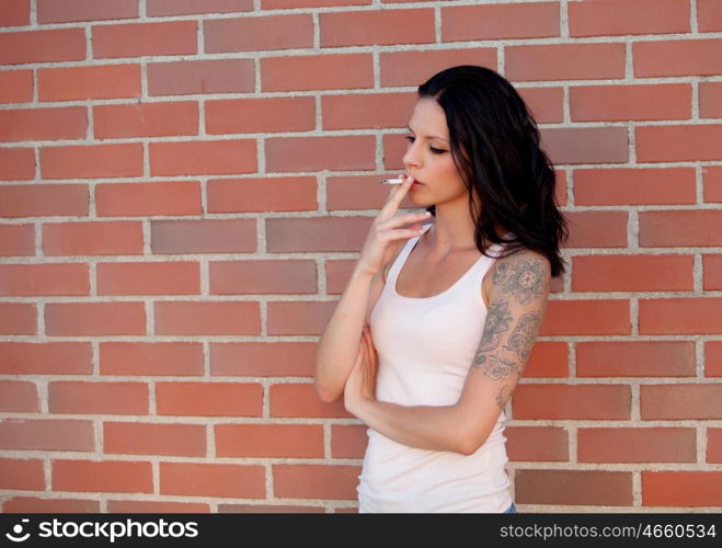 Rebel brunette woman with tight shirt smoking a cigarette on background of red bricks