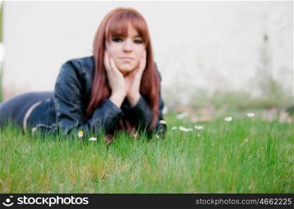Rebellious teenager girl with red hair lying on the grass. Focus in grass