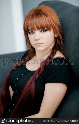 Rebellious teenager girl with red hair sit on the sofa