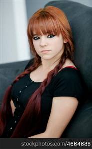 Rebellious teenager girl with red hair sit on the sofa