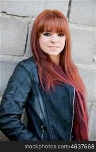 Rebellious teenager girl with red hair smiling and leaning on a wall
