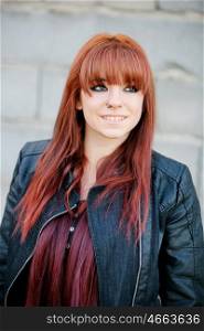 Rebellious teenager girl with red hair smiling and leaning on a wall