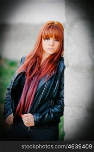 Rebellious teenager girl with red hair very sad leaning on a wall