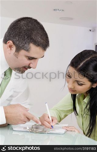 Receptionist writing on a clipboard with a businessman talking to her