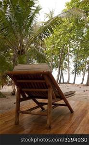 Reclining wood lounge chair on a wooden deck facing jungle trees