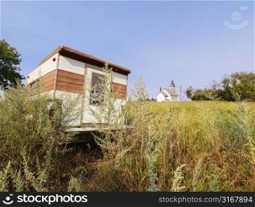 Recreational vehicle in overgrown field with rural church in distance.