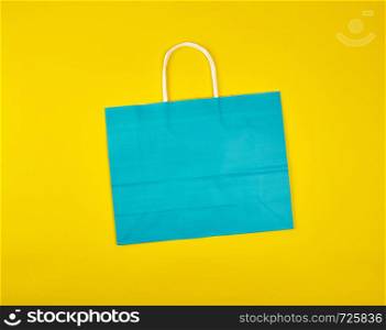 rectangular blue paper shopping bag with a white handle on a yellow background, flat lay
