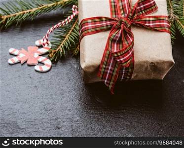 rectangular box wrapped in brown paper and tied with a red silk ribbon with a bow, gift on a black background, close up