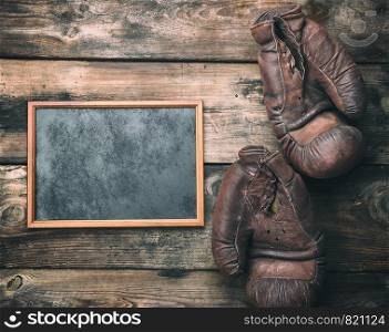 rectangular brown wooden frame and very old leather boxing gloves on a plank background