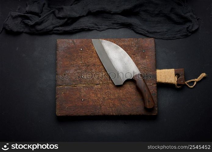 Rectangular empty wooden cutting board and kitchen knife on black table with gauze napkin, top view