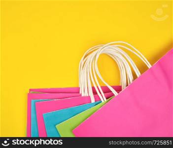 rectangular multi-colored paper shopping bags with white handles on a yellow background, flat lay