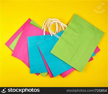 rectangular multi-colored paper shopping bags with white handles on a yellow background, flat lay