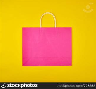 rectangular pink paper shopping bag with a white handle on a yellow background, flat lay