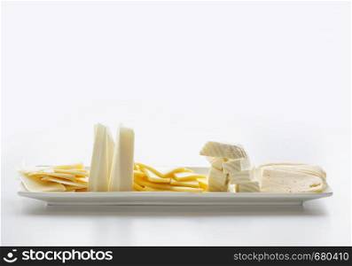Rectangular white porcelain plate, filled with pieces of cheese of different varieties with copy-space. Side view