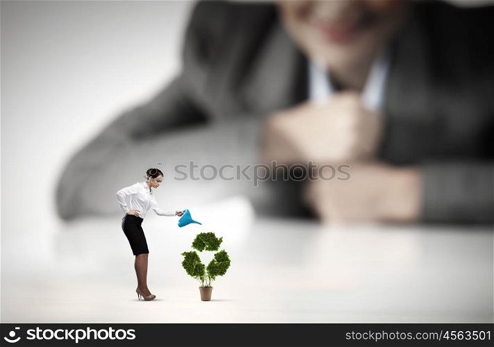 Recycle concept. Businesswoman looking at miniature of woman watering plant
