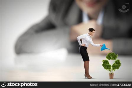 Recycle concept. Businesswoman looking at miniature of woman watering plant