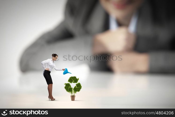 Recycle concept. Businesswoman looking at miniature of woman watering plant