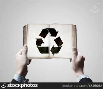 Recycle concept. Close up f male hands holding opened book with recycle sign