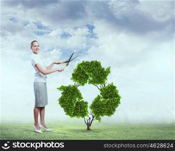 Recycle concept. Young attractive businesswoman cutting plant in shape of recycle symbol