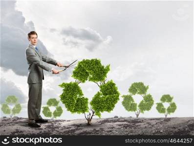 Recycle concept. Young businessman cutting bush in shape of recycle symbol
