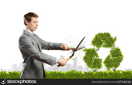Recycle concept. Young businessman cutting bush in shape of recycle symbol