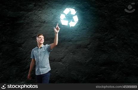 Recycle concept. Young handsome man against dark backdrop touching recycle sign