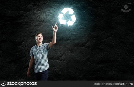 Recycle concept. Young handsome man against dark backdrop touching recycle sign