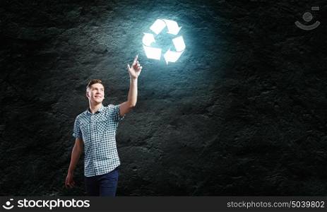 Recycle concept. Young handsome man against dark backdrop touching recycle sign