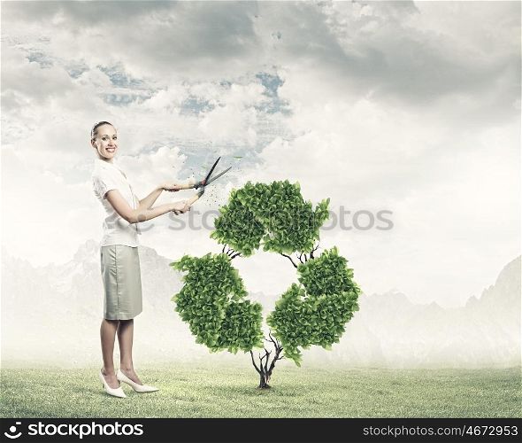 Recycle concept. Young smiling businesswoman cutting plant in shape of recycle sign