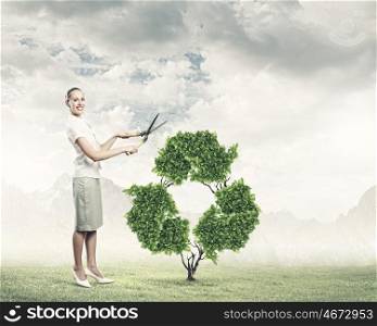 Recycle concept. Young smiling businesswoman cutting plant in shape of recycle sign