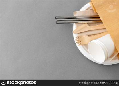 recycling and eco friendly concept - set of wooden forks, knives, paper cups and metallic straws with napkin on plate on grey background. wooden forks, knives and paper cups on plate