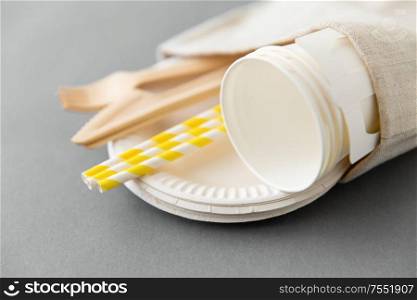 recycling and eco friendly concept - wooden disposable forks, knives, paper cups and straws with canvas napkin on grey background. wooden forks, knives, paper straws and cups