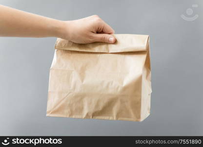 recycling and ecology concept - hand holding disposable brown takeaway food in paper bag with lunch on table. hand holding takeaway food in paper bag with lunch