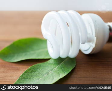 recycling, electricity, environment and ecology concept - close up of energy saving lighting bulb on wooden boards and green leaf