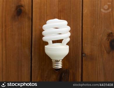 recycling, electricity, environment and ecology concept - close up of energy saving lighting bulb on wooden boards
