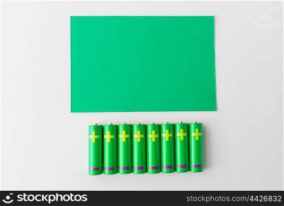 recycling, energy, power, environment and ecology concept - close up of green alkaline batteries and blank paper