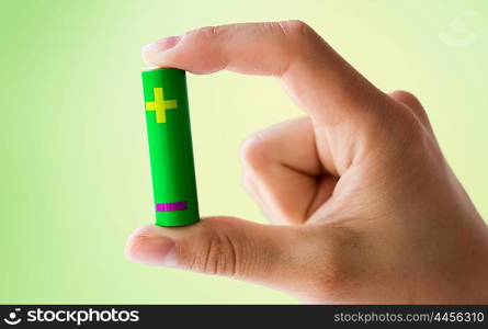 recycling, energy, power, environment and ecology concept - close up of hand holding green alkaline battery over green background