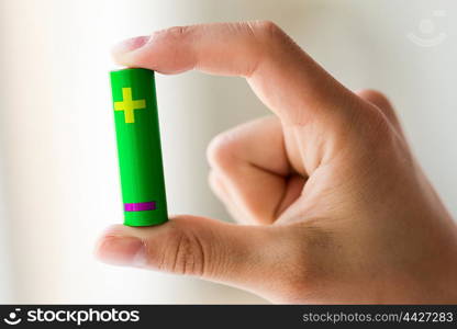 recycling, energy, power, environment and ecology concept - close up of hand holding green alkaline battery