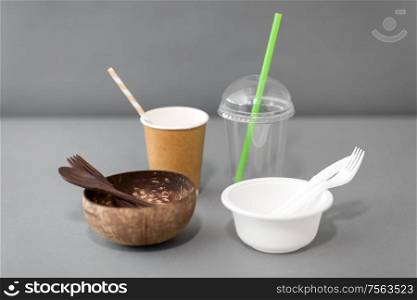 recycling, environment and eco friendly concept - close up of natural coconut bowl with wooden spoon and fork and plastic dishes on table. close up of eco friendly and plastic tableware