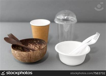 recycling, environment and eco friendly concept - close up of natural coconut bowl with wooden spoon and fork and plastic dishes on table. close up of eco friendly and plastic tableware
