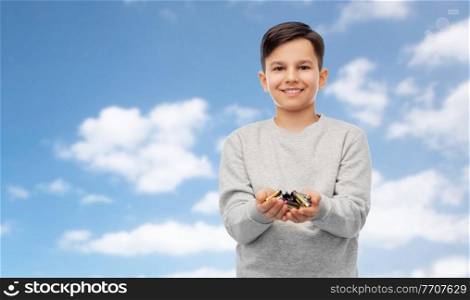 recycling, environment and ecology concept - smiling boy holding pile of alkaline batteries over blue sky and clouds background. smiling boy holding pile of alkaline batteries
