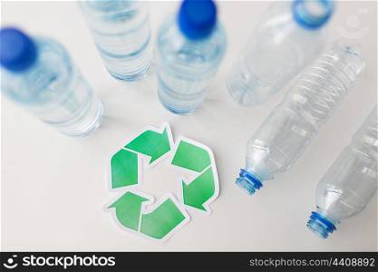 recycling, reuse, garbage disposal, environment and ecology concept - close up of empty plastic water bottles with green recycle symbol on table