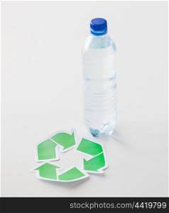 recycling, reuse, garbage disposal, environment and ecology concept - close up of plastic water bottle with green recycle symbol on table