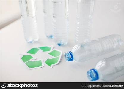 recycling, reuse, garbage disposal, environment and ecology concept - close up of empty plastic water bottles with green recycle symbol on table