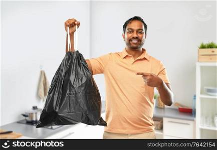 recycling, sorting and sustainability concept - smiling young indian man holding trash bag over home kitchen background. smiling indian man holding trash bag