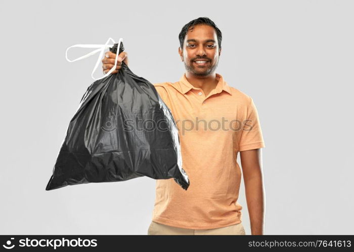 recycling, sorting and sustainability concept - smiling young indian man holding trash bag over grey background. smiling indian man holding trash bag