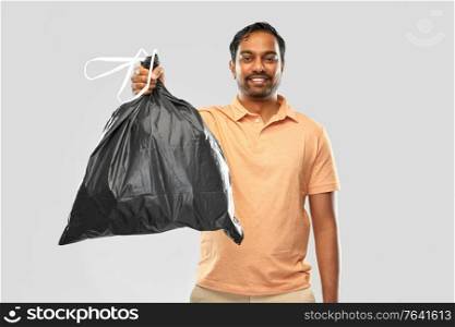 recycling, sorting and sustainability concept - smiling young indian man holding trash bag over grey background. smiling indian man holding trash bag