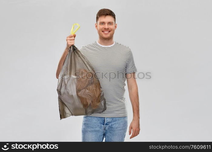 recycling, sorting and sustainability concept - smiling young man in striped t-shirt holding trash bag with paper waste over grey background. smiling man holding trash bag with paper waste