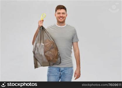 recycling, sorting and sustainability concept - smiling young man in striped t-shirt holding trash bag with paper waste over grey background. smiling man holding trash bag with paper waste
