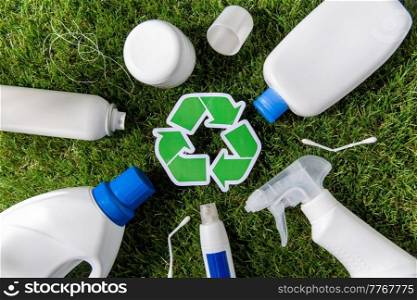 recycling, sustainability and ecology concept - close up of plastic and household chemicals waste with green recycle symbol on grass. close up of plastic waste and recycling sign